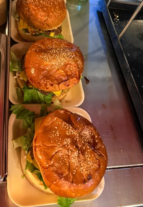 Tres hamburguesas recién armadas en fila sobre la barra del puesto